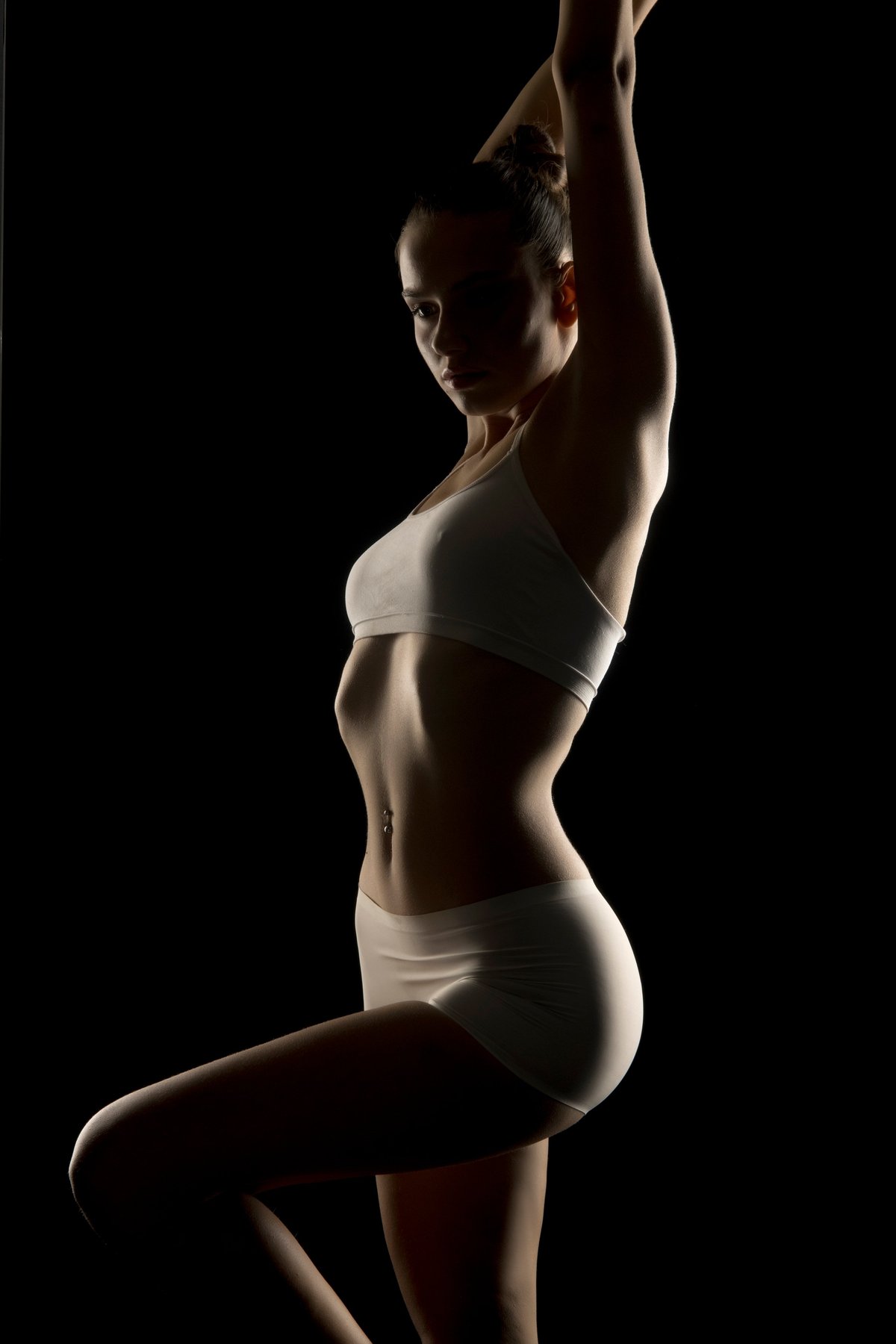 Dramatic silhouette of a young woman in underwear, body arched backwards. Dark background with rim lighting highlighting curves. Artistic photography concept