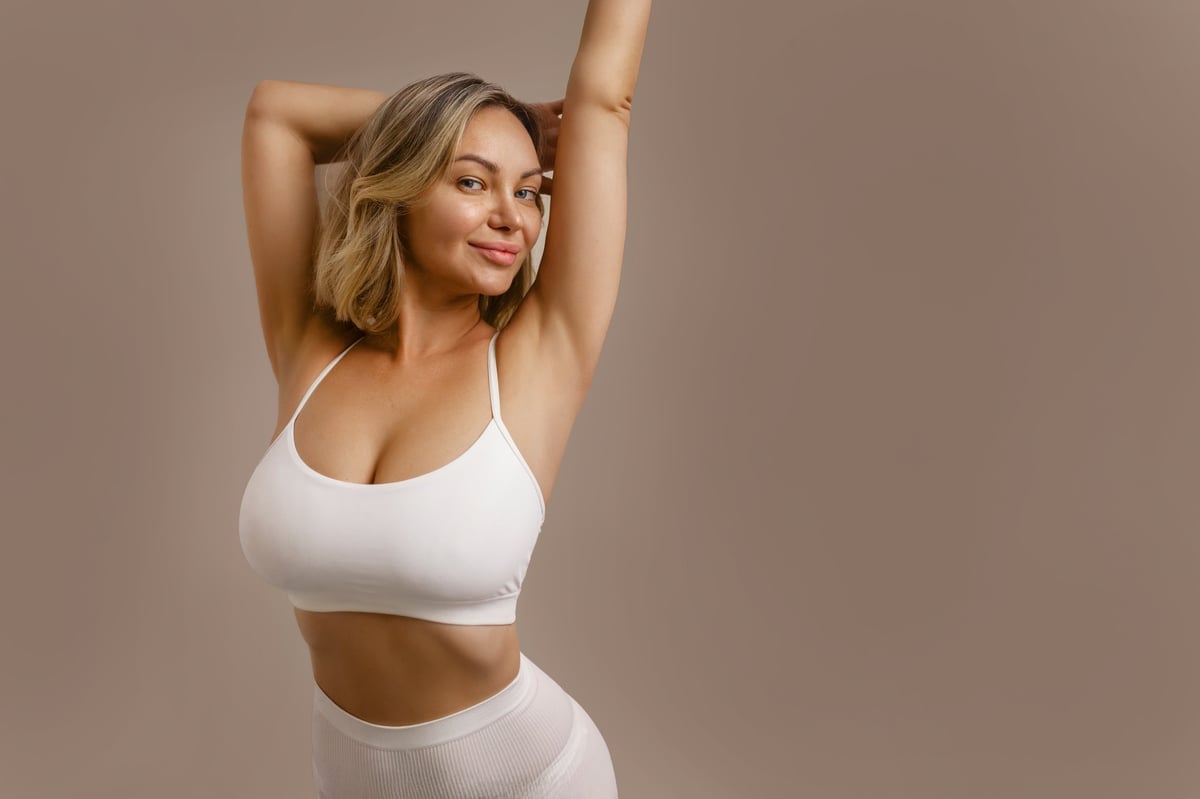 Young beautiful woman in white lingerie, smiling and touching her body, showing natural beauty, body positivity and healthy lifestyle on beige background