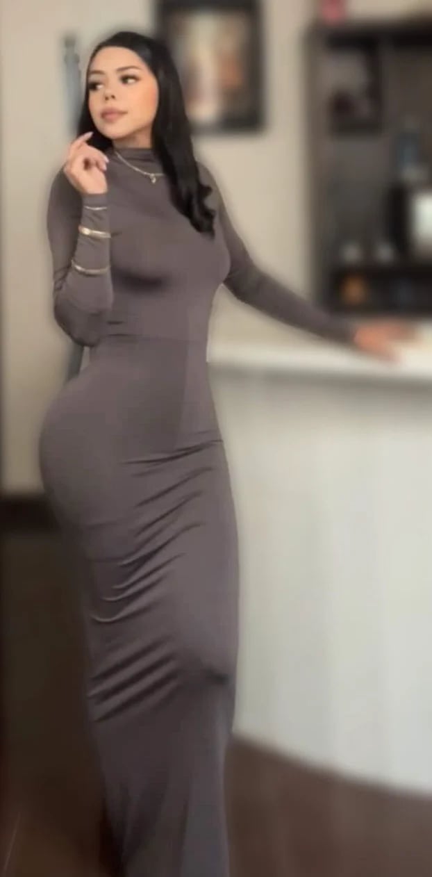 Woman in gray long-sleeve turtleneck dress with cutout details poses indoors, looking to the side