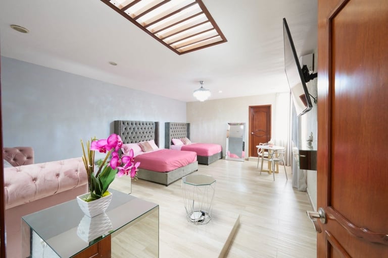 Modern bedroom suite with pink bedding, wooden furnishings, skylight, pink orchid flowers on desk, and mounted TV on wall